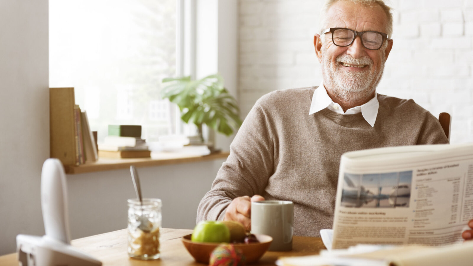 A senior male is reading his newspaper in the morning while enjoying a cup of coffee to keep his morning routine.