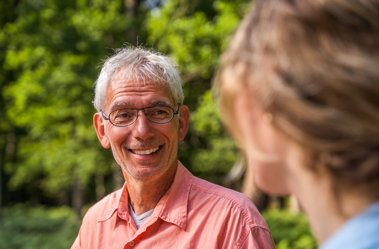 A senior man and his daughter smiling and talking to each other in a park.