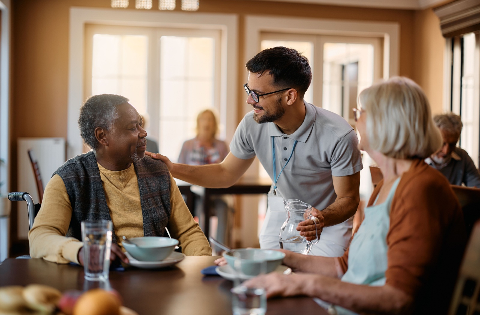 Senior living Aide offering water to two seniors during breakfast.