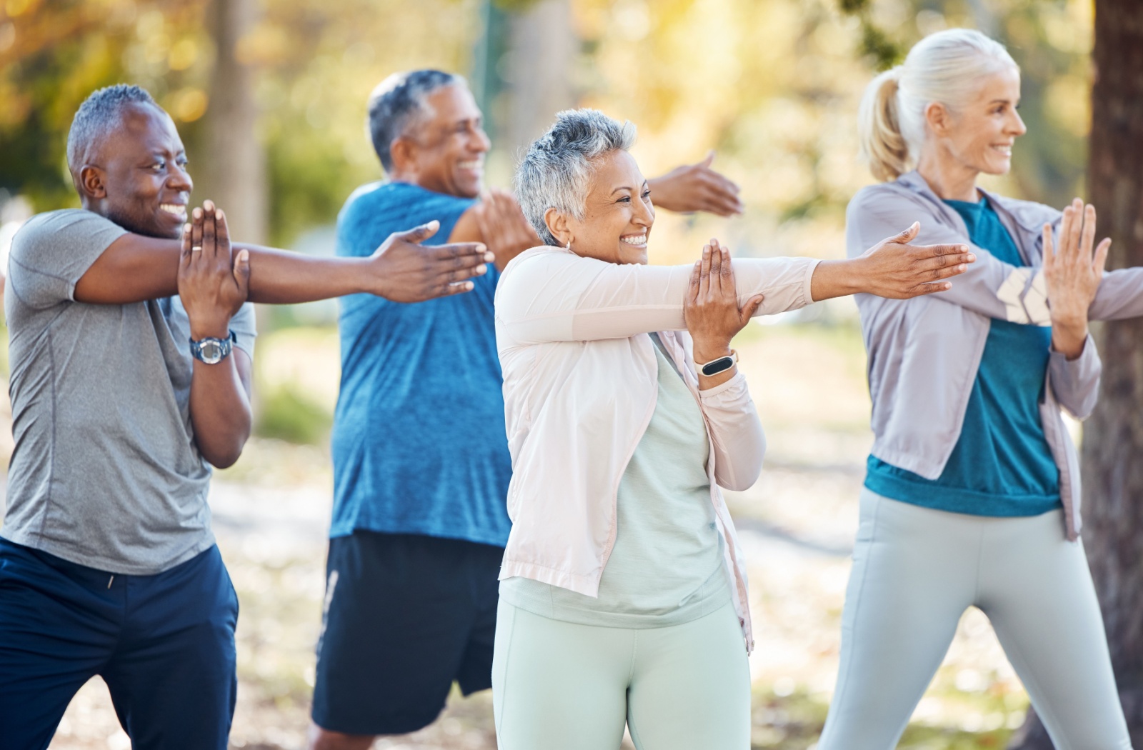 Group of older adults doing gentle arm stretches together outdoors.