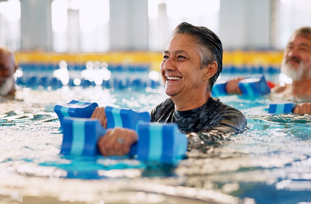 An older adult smiling while participating in a water aerobics class.