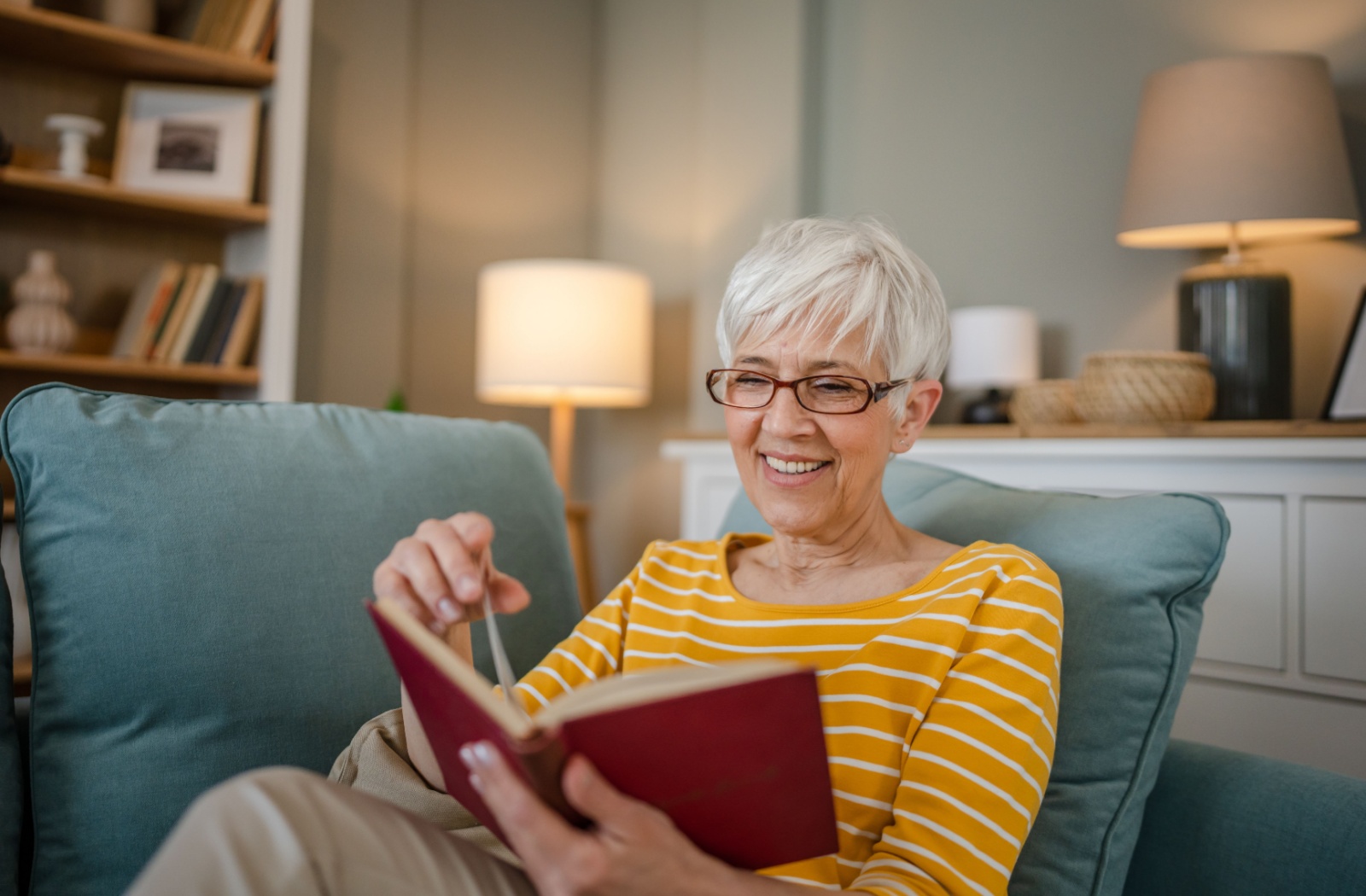 An older adult reads a book while lounging on a comfortable couch.