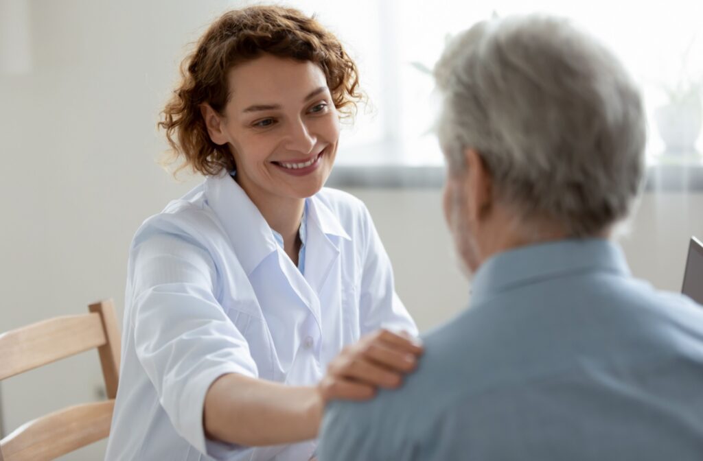 Smiling healthcare provider placing a reassuring hand on an older adult’s shoulder.