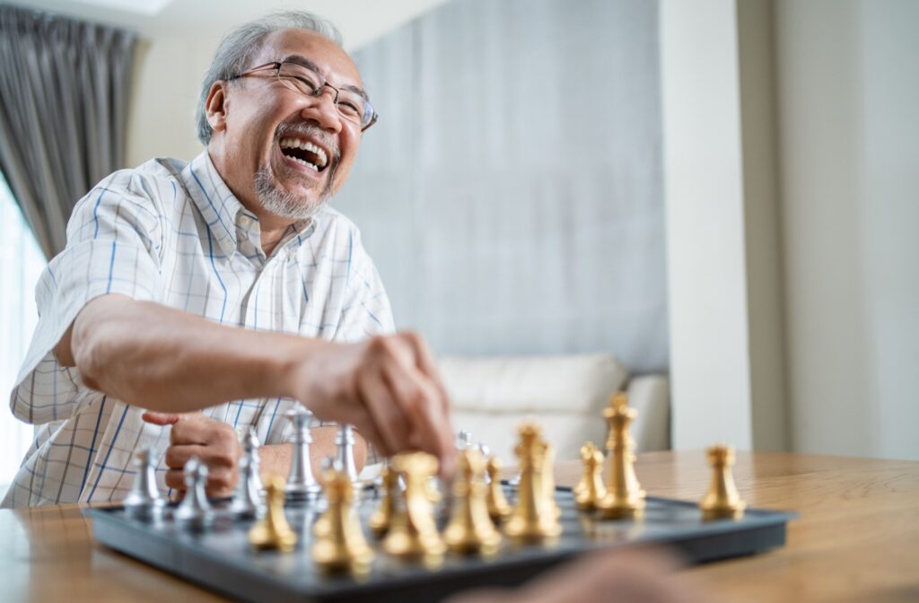 An older adult laughing while moving a chess piece during a fun game in senior living.