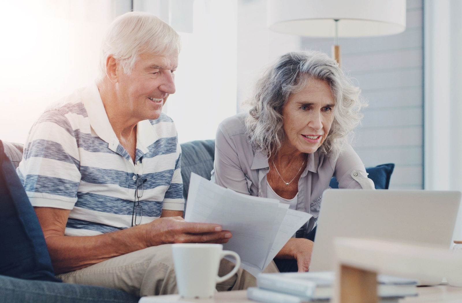 A senior couple looks at a laptop and paperwork as they fill out an application form for assisted living.
