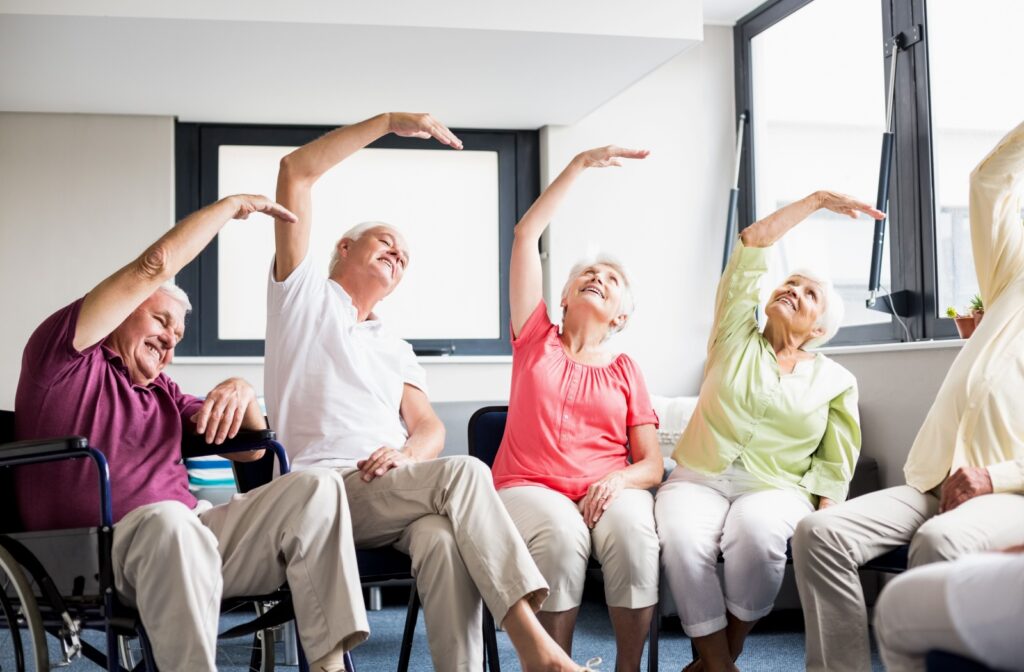 In a communal senior living space, a group of seniors stretch their arms together to encourage community fitness and wellness